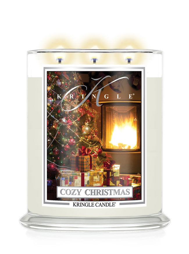 A Kringle Candle in a clear glass jar with three lit wicks, featuring a festive 'Cozy Christmas' label with a warm fireplace and decorated Christmas tree scene.