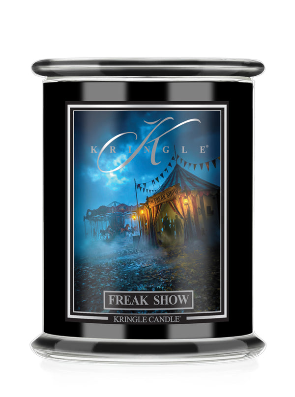 A black glass jar candle featuring a front label for Kringle Candle Halloween scent 'Freak Show' with an illustration of a circus tent at night.