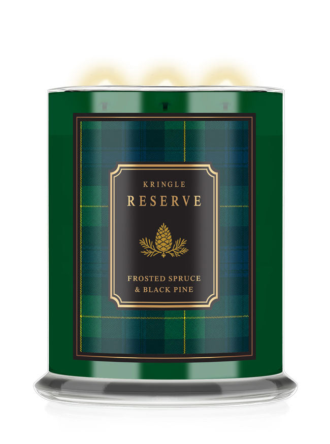 A Kringle Reserve candle in a cylindrical green tin with a black and gold label reading 'Frosted Spruce & Black Pine,' shown on a white background with warm light glowing from the top wicks.