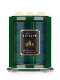 A Kringle Reserve candle in a cylindrical green tin with a black and gold label reading 'Frosted Spruce & Black Pine,' shown on a white background with warm light glowing from the top wicks.