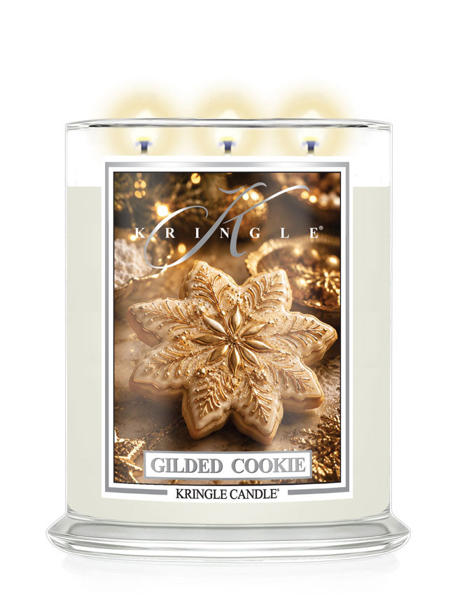 A Kringle Candle in a clear glass jar with three lit wicks, featuring a label that reads 'Gilded Cookie' and shows a decorated cookie on a warm gold holiday background.