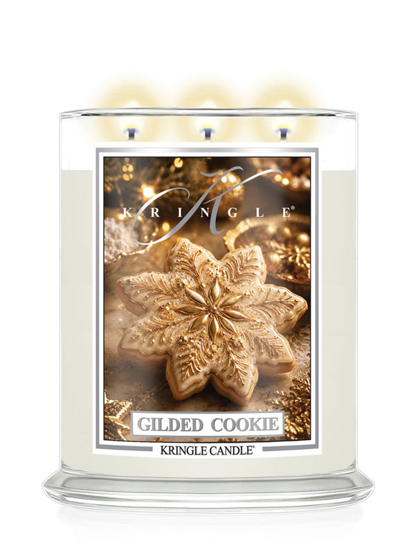 A Kringle Candle in a clear glass jar with three lit wicks, featuring a label that reads 'Gilded Cookie' and shows a decorated cookie on a warm gold holiday background.