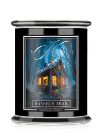 A black glass jar Halloween candle featuring a front label for 'Kringle Candle' titled 'Hansel's Trail'. The label shows a whimsical, glowing haunted house surrounded by colorful candy-like shapes in a dark blue forest.