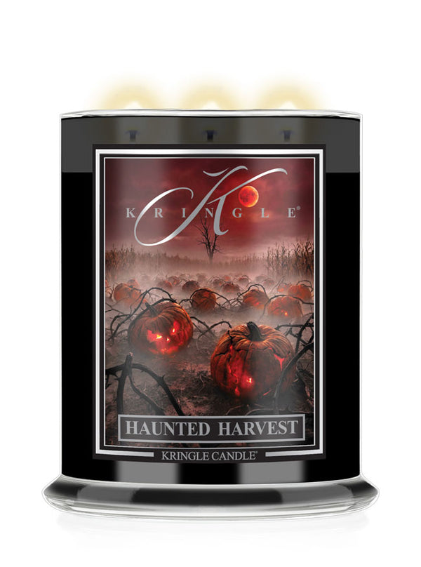 A Kringle Candle in a tall black jar with three lit wicks, featuring a Halloween-themed label that reads 'Haunted Harvest' and shows glowing red pumpkins in a misty field under a red sky.