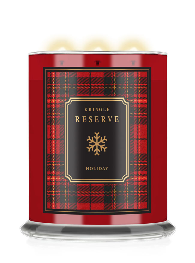 A Kringle Reserve Holiday scented candle in a cylindrical glass jar with a red and black tartan plaid label, featuring a gold snowflake logo and three lit wicks at the top.