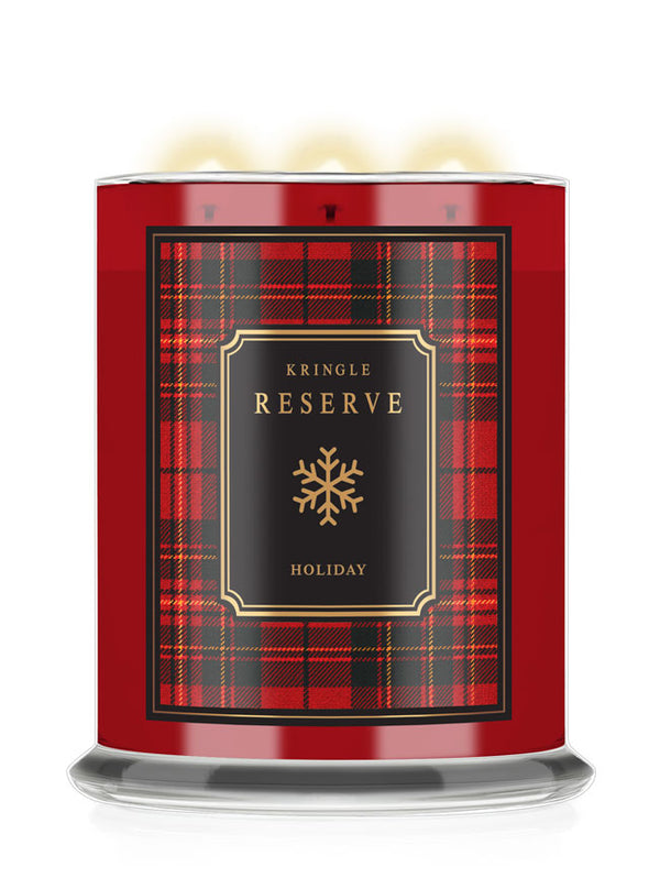 A Kringle Reserve Holiday scented candle in a cylindrical glass jar with a red and black tartan plaid label, featuring a gold snowflake logo and three lit wicks at the top.