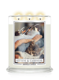 A Kringle Candle in a clear glass jar with a white wax fill and a front label depicting a kitten in a pile of soft sweaters. The label reads 'KRINGLE', 'Kittens and Cashmere, and 'KRINGLE CANDLE'.