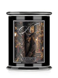 A Kringle Candle Halloween jar with a black glass body, featuring a detailed label of a hairy creature in a festive town scene, labeled 'Krampus'.