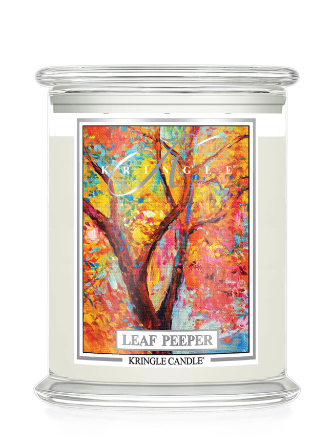 A Kringle Candle jar candle with a clear glass lid and base, filled with off-white wax and featuring a colorful label of a tree with autumn leaves. The label reads 'LEAF PEEPER' and 'KRINGLE CANDLE'.