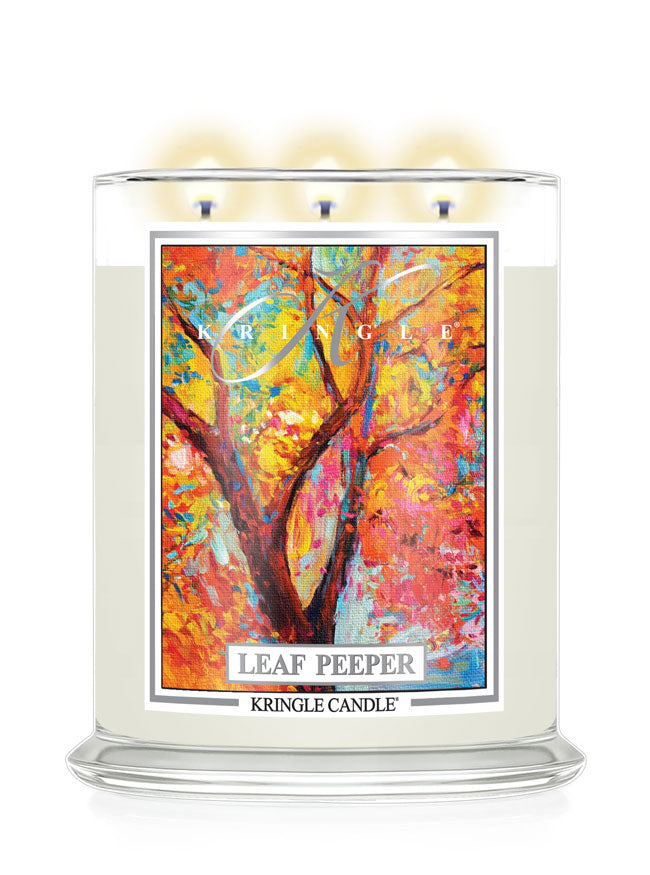 A Kringle Candle 'Leaf Peeper' three-wick soy candle in a clear glass jar with a colorful autumn tree illustration on the front label, shown lit against a white background.