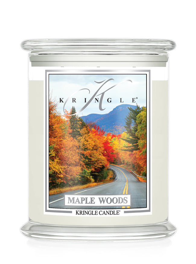 A Kringle Candle in a clear glass jar with three wicks and lid, featuring a label that depicts a scenic autumn road through maple woods with mountains in the background. 