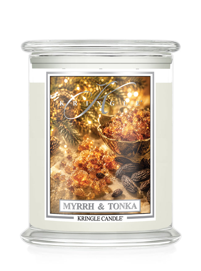 A Kringle Candle jar candle with a clear glass lid and base, filled with creamy off-white wax. The front label features a warm, festive design with amber myrrh resin, cinnamon sticks, and pine branches, and the text 'MYRRH & TONKA' and 'KRINGLE CANDLE'.