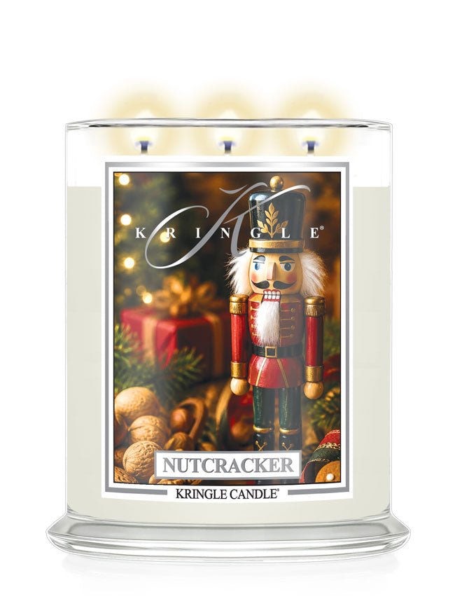 A large three-wick holiday candle in a clear glass jar with a white wax body and a festive front label featuring a nutcracker, ornaments, and the text 'Kringle' and 'Nutcracker' by Kringle Candle.