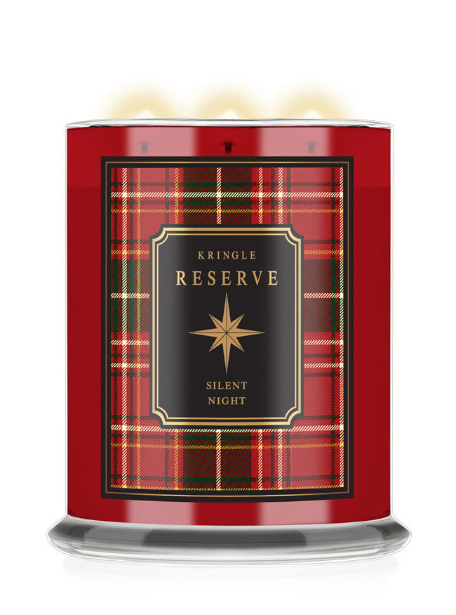 A Kringle Reserve 'Silent Night' scented candle in a red glass jar with a black and red tartan label, featuring three lit wicks and a clear glass base.