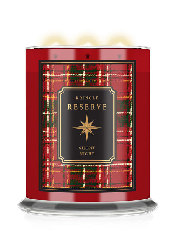 A Kringle Reserve 'Silent Night' scented candle in a red glass jar with a black and red tartan label, featuring three lit wicks and a clear glass base.