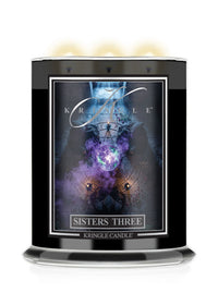 A black glass jar candle  with 3 lit wicks for Kringle Candle's 'Sisters Three' Halloween scent. The label displays a dark, mystical graphic with purple and blue cosmic elements.