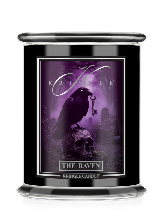A black glass jar candle featuring a gothic label for 'Kringle Candle' titled 'The Raven'. The label depicts a black raven perched on a skull holding a key in a purple misty graveyard scene.