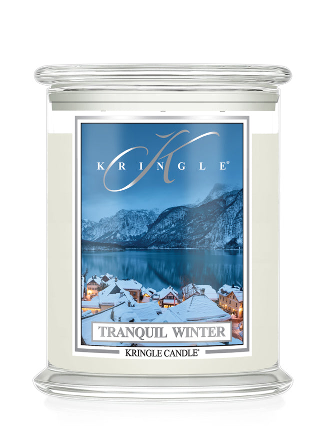 A Kringle Candle in a clear glass jar  featuring a winter landscape label that reads 'Tranquil Winter' and shows snowy rooftops, mountains, and a blue lake.