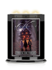 A Kringle Candle 'Trick or Treat' scented candle in a tall black glass jar with three lit wicks at the top, featuring a Halloween-themed label illustration of children facing a haunted house.