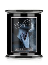 A black glass jar Halloween candle featuring a Halloween-themed label titled 'Vampire's Kiss' by Kringle Candle. The label depicts a pale figure with a hand near their neck with red "bites", set against a dark smoky background.