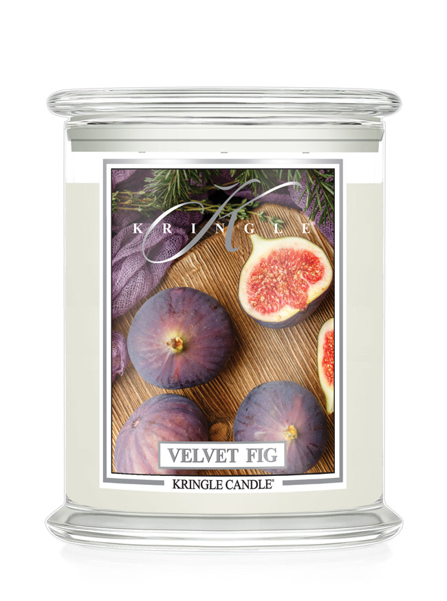 A Kringle Candle jar candle labeled 'Velvet Fig' with a clear glass container, cream-colored wax, and a front label showing purple figs and a halved fig on a wooden surface.