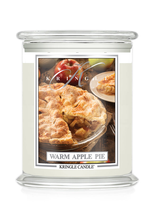 A Kringle Candle jar candle with a clear glass lid and base, filled with off-white wax and featuring a front label that reads 'Warm Apple Pie' with a photo of an apple pie, on a white background.
