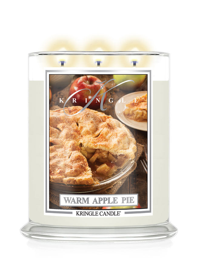 A three-wick Kringle Candle in a clear glass jar with cream-colored wax and a front label reading 'Warm Apple Pie.' The label shows an apple pie photo with apples and a plate of pie.