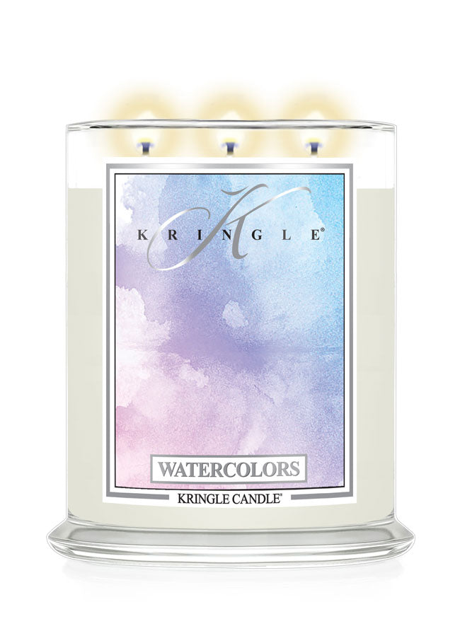 A three-wick Kringle Candle in a clear glass jar with cream-colored wax and a colorful watercolor label reading 'WATERCOLORS' and 'KRINGLE CANDLE'. The top of the candle shows three lit flames against a white background.