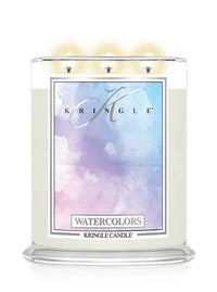 A three-wick Kringle Candle in a clear glass jar with cream-colored wax and a colorful watercolor label reading 'WATERCOLORS' and 'KRINGLE CANDLE'. The top of the candle shows three lit flames against a white background.