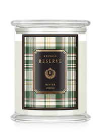 A Kringle Reserve 'Winter Lodge' scented candle in a clear glass jar with a lid, featuring a green and beige plaid label with a black central panel and gold lettering.