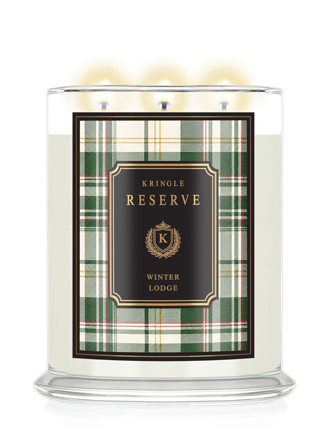 A three-wick scented candle in a clear glass jar with lit flames, featuring a green and white plaid label with a black center panel that reads 'KRINGLE RESERVE WINTER LODGE' in gold lettering.
