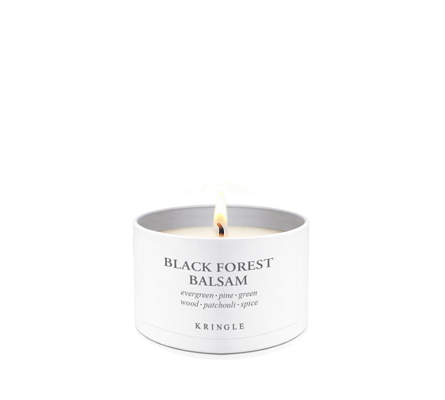A lit white candle in a white cylindrical tin labeled 'BLACK FOREST BALSAM' with the brand 'KRINGLE' visible, centered on a clean white background.
