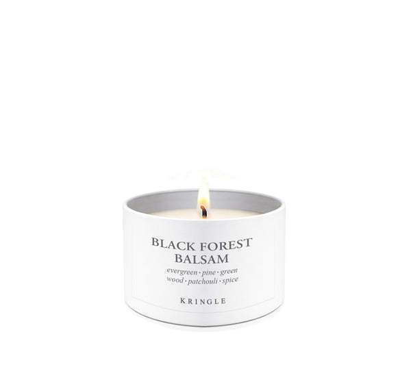 A lit white candle in a white cylindrical tin labeled 'BLACK FOREST BALSAM' with the brand 'KRINGLE' visible, centered on a clean white background.