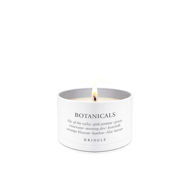 A lit Kringle Botanicals scented candle in a white cylindrical metal tin shown against a seamless white background.