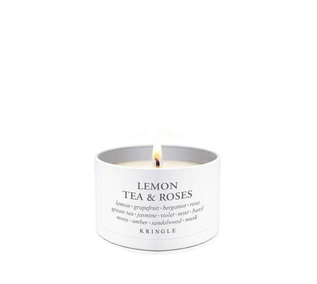 A lit white candle in a white cylindrical tin with the text 'LEMON TEA & ROSES' and the brand 'KRINGLE' printed on the front, set against a solid white background.