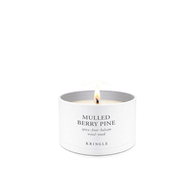 A lit white candle in a cylindrical white metal tin with the text 'MULLED BERRY PINE' and 'KRINGLE' printed on the front, set against a solid white background.
