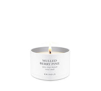 A lit white candle in a cylindrical white metal tin with the text 'MULLED BERRY PINE' and 'KRINGLE' printed on the front, set against a solid white background.