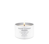 A lit white candle in a cylindrical white tin with the text 'SNOW-CAPPED FRASER' and 'KRINGLE' printed on the front, set against a solid white background.