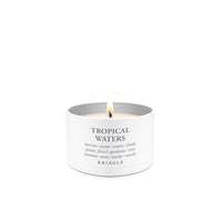 A white metal candle tin with a single lit flame, labeled 'TROPICAL WATERS' by the brand KRINGLE, on a seamless white background.