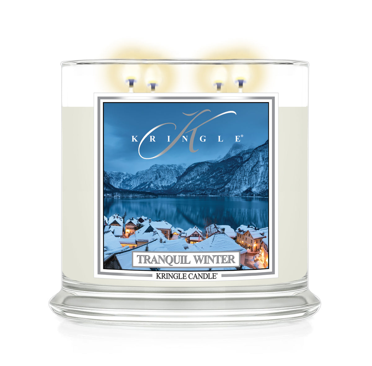 A Kringle Candle in a clear glass jar with three lit wicks, featuring a winter landscape label that reads 'Tranquil Winter' and shows snowy rooftops, mountains, and a blue lake.