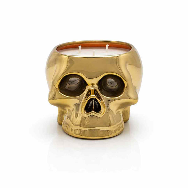 A gold skull-shaped candle holder with a glossy metallic finish, featuring a visible orange wax interior, set against a clean white background.