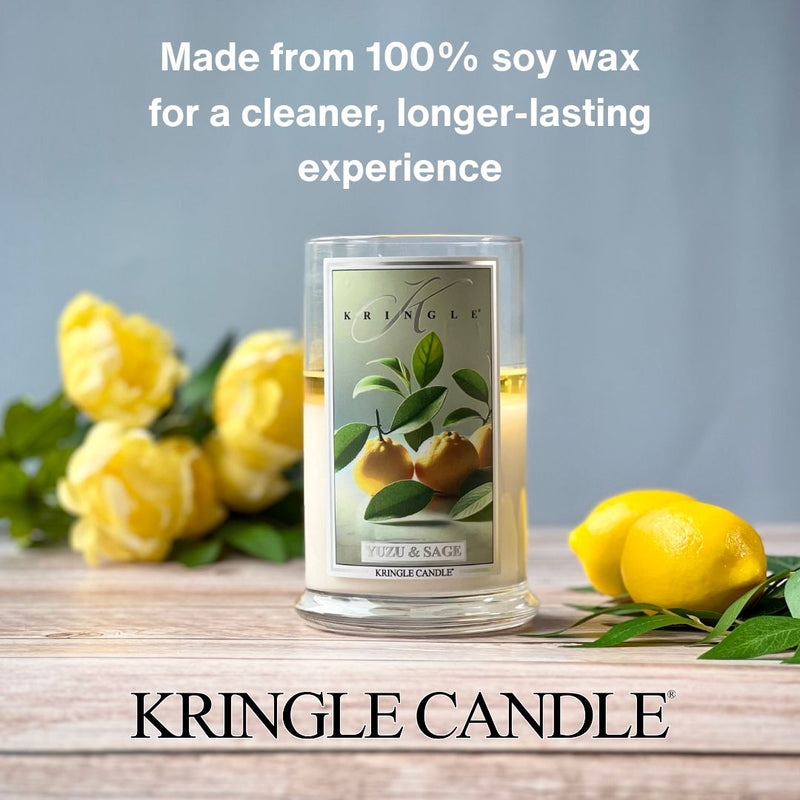 Kringle Candle’s Yuzu & Sage 2-wick jar candle displayed on a wooden surface, surrounded by fresh lemons and yellow roses, with text above reading “Made from 100% soy wax for a cleaner, longer-lasting experience.”