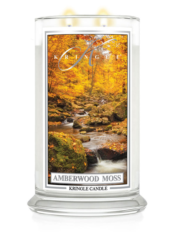Amberwood Moss candle with two lit wicks. Label shows a forest scene with a rocky stream surrounded by autumn trees.