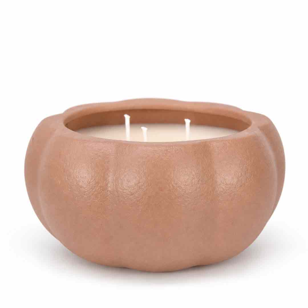 A three-wick candle in a matte, pumpkin-shaped ceramic container with a warm terracotta or light brown finish, set against a plain white background.