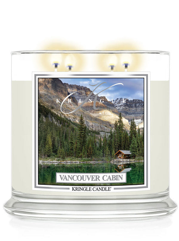 Four-wick candle lit, featuring a scenic label of a lakeside cabin surrounded by trees and mountains,  "Vancouver Cabin"