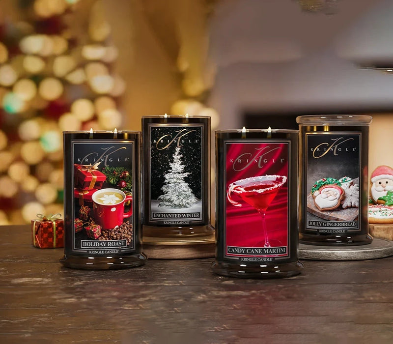 Four scented candles with decorative labels on a wooden surface, blurred Christmas lights in the background.