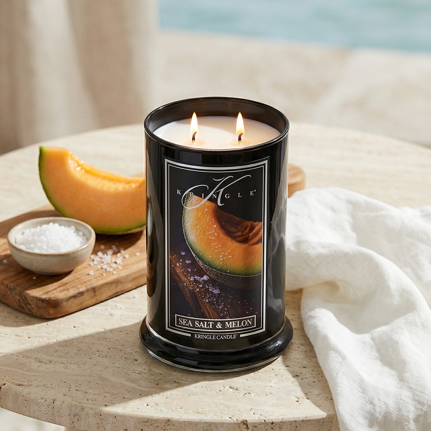 Candle with a melon design on the label, placed on a surface with a melon and salt.