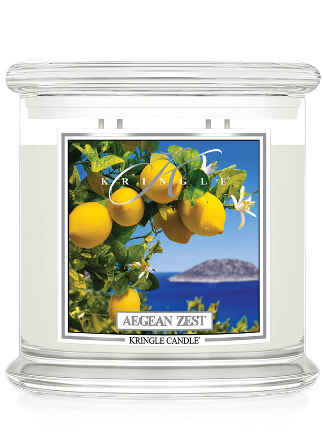 Kringle Candle Aegean Zest 4-Wick Jar Candle – A large, clear glass jar candle with a matching glass lid, filled with white wax. The label features bright yellow lemons, green leaves, and white blossoms with a scenic deep blue ocean and an island in the background. The ‘Kringle Candle’ logo is at the top, with the fragrance name ‘Aegean Zest’ in bold, and ‘Kringle Candle’ branding at the bottom.