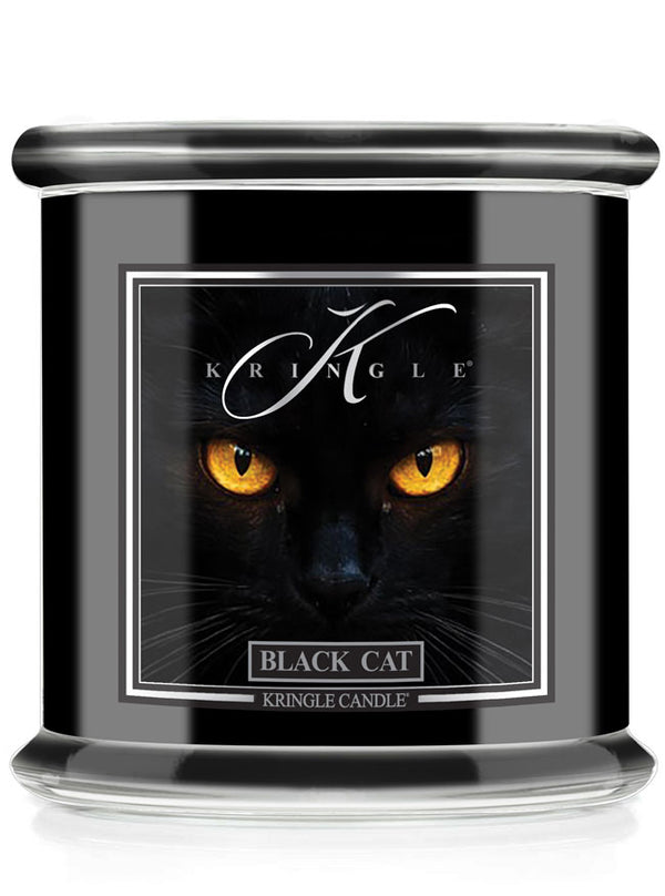 A Kringle Candle jar candle labeled 'Black Cat' featuring a graphic of a black cat's face with glowing yellow eyes on a black container with a silver lid.