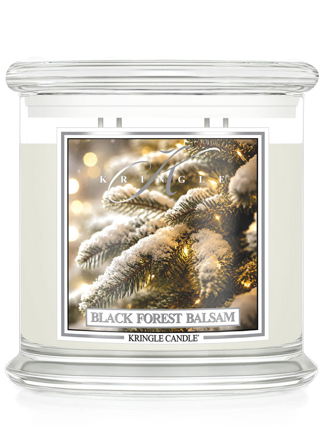 A Kringle Candle jar candle labeled 'Black Forest Balsam' with a frosted glass container, cream-colored wax, and a front label showing snowy pine branches with warm lights.